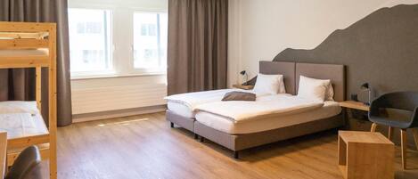 Una habitación de hotel moderna con una cama grande, una cama nido de madera, un escritorio y una silla.