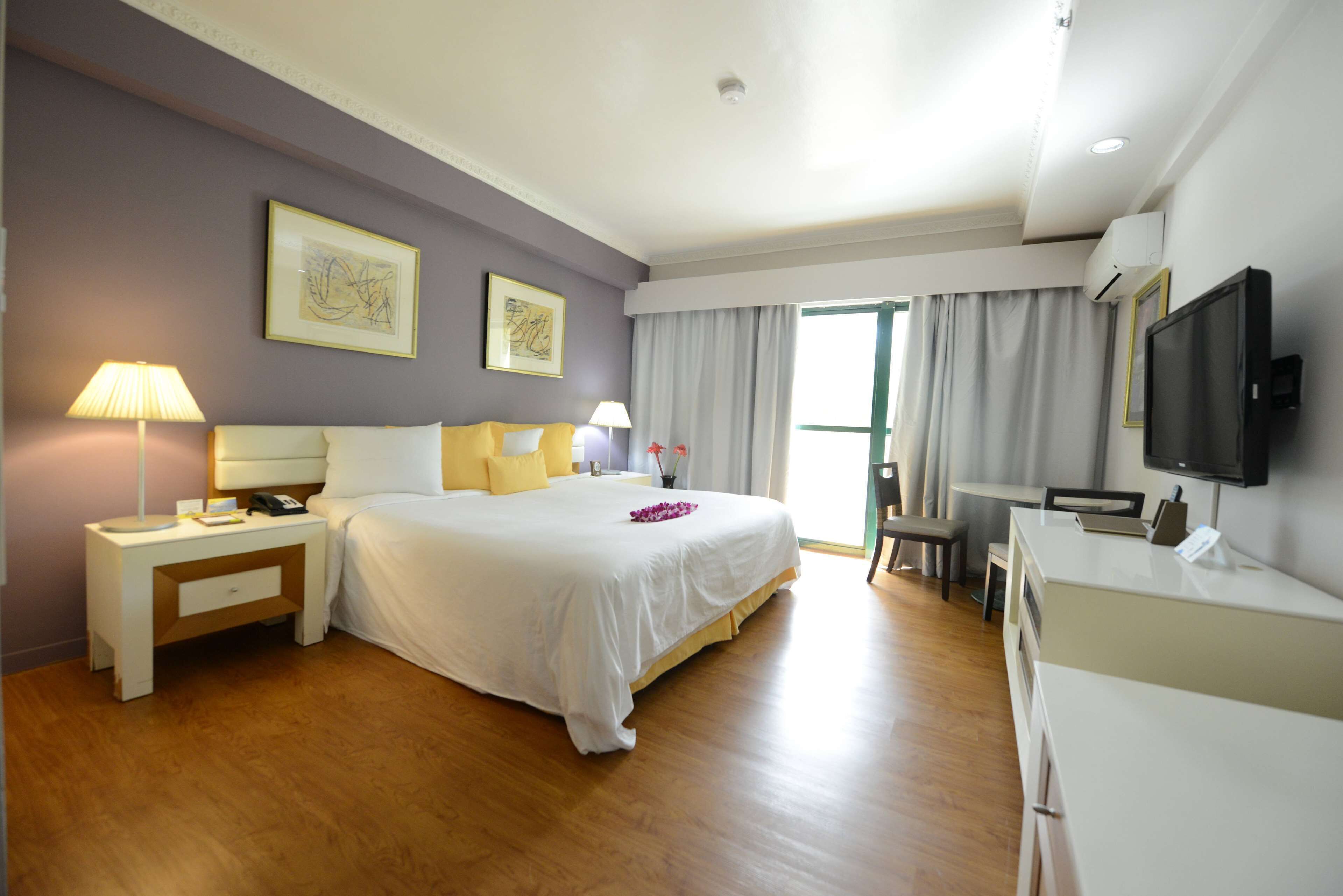 Habitación de hotel con una cama grande, mesitas de noche, un escritorio, una silla, un televisor y una ventana con cortinas.