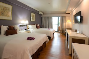 A hotel room with two beds, a desk, a TV, and a large window.