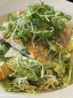 Un plato de comida con salmón, verduras de hoja y brotes.