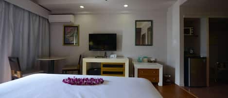 A hotel room with a large bed, a desk with a computer, a television, a mirror, and a kitchenette.
