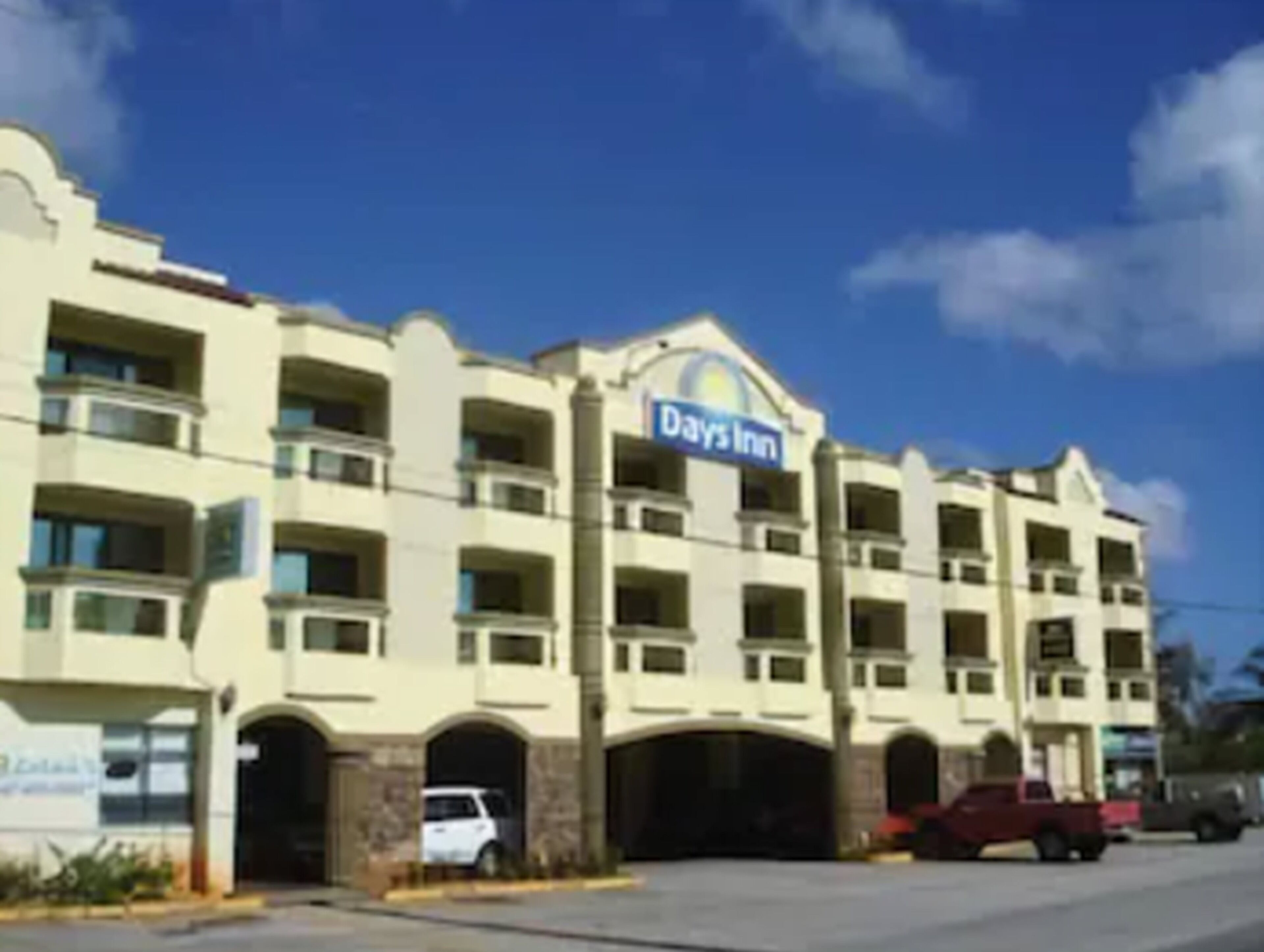 Een meerlaags hotel met een Days Inn bord, meerdere balkons en een parkeerplaats met auto's.