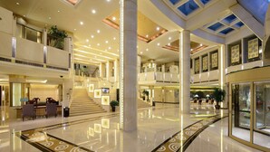 A spacious, multi-level atrium with a polished floor, a central staircase, and a seating area with tables and chairs. - Ramada Plaza Taian (Tai'an)