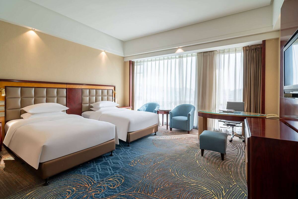 A hotel room with two beds, a desk, a chair, and a TV.