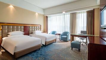 A hotel room with two beds, a desk, a chair, and a TV.