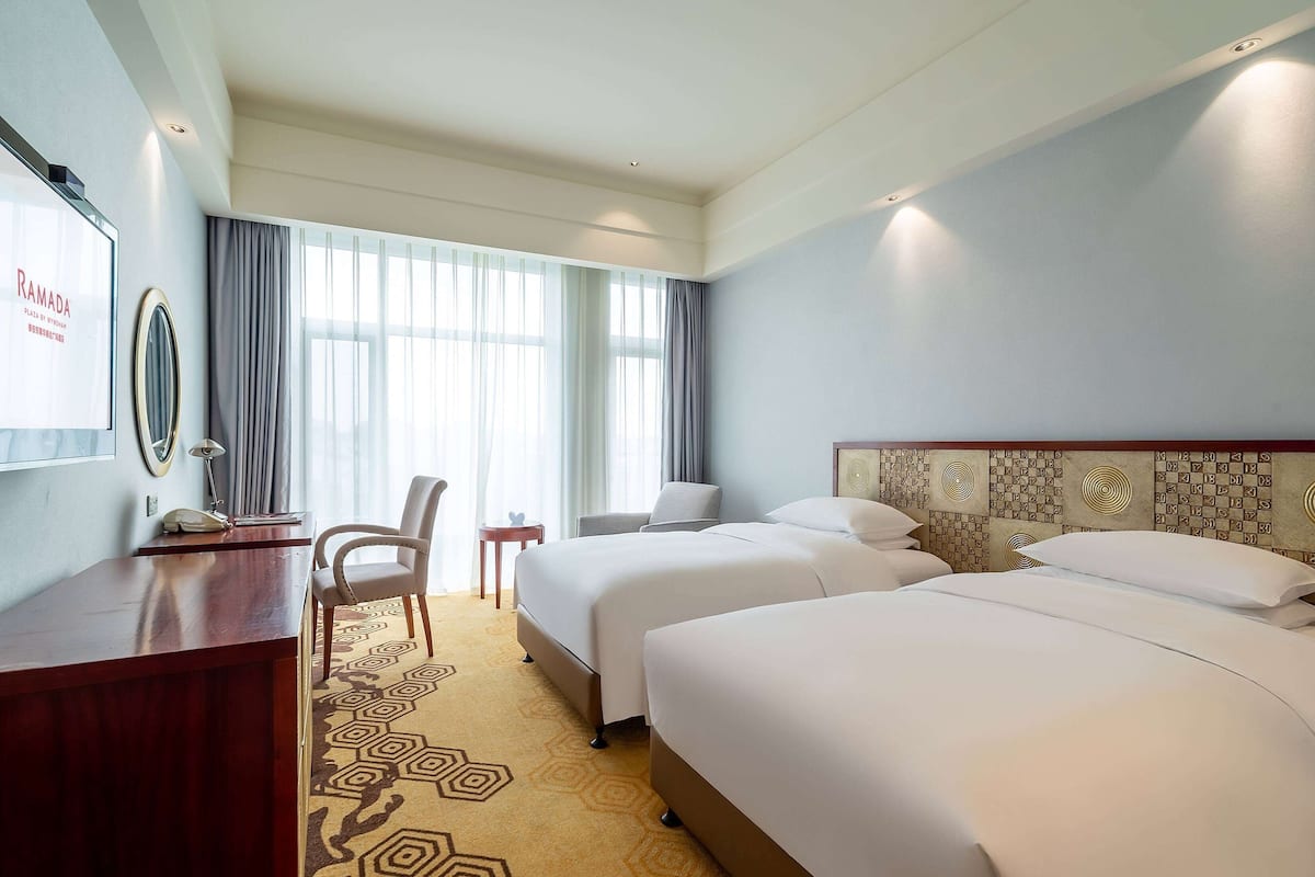 A hotel room with two beds, a desk, a chair, and a large window with curtains.