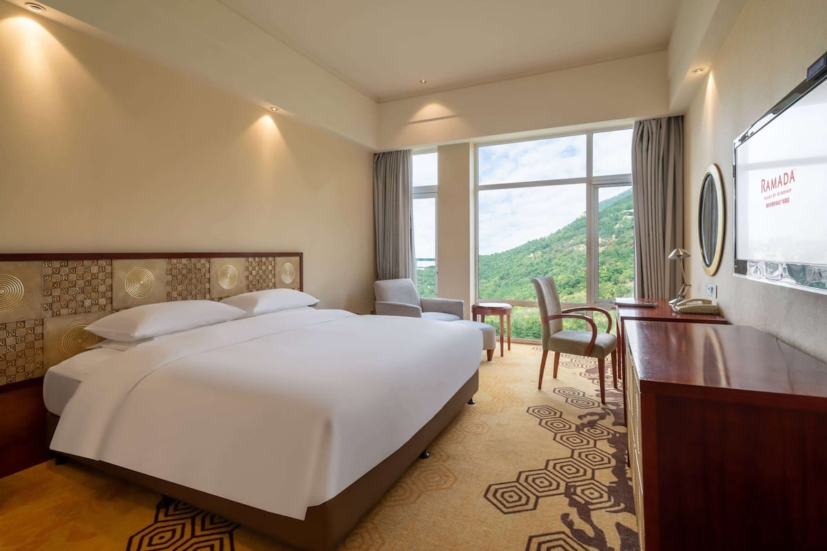 A hotel room with a large bed, a desk, a chair, and a view of the outdoors.