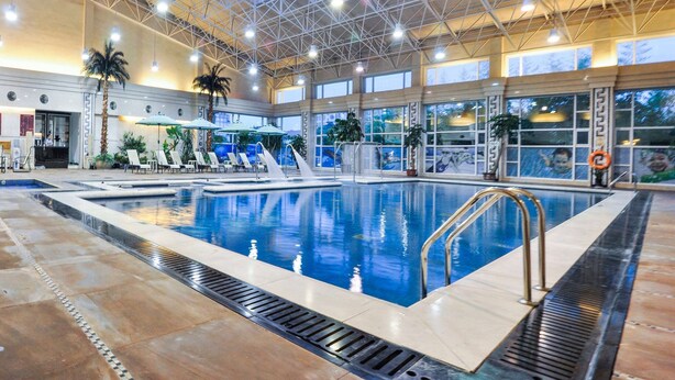 An indoor swimming pool with a high ceiling, multiple lounge chairs, and a water slide. - Ramada Plaza Taian (Tai'an)