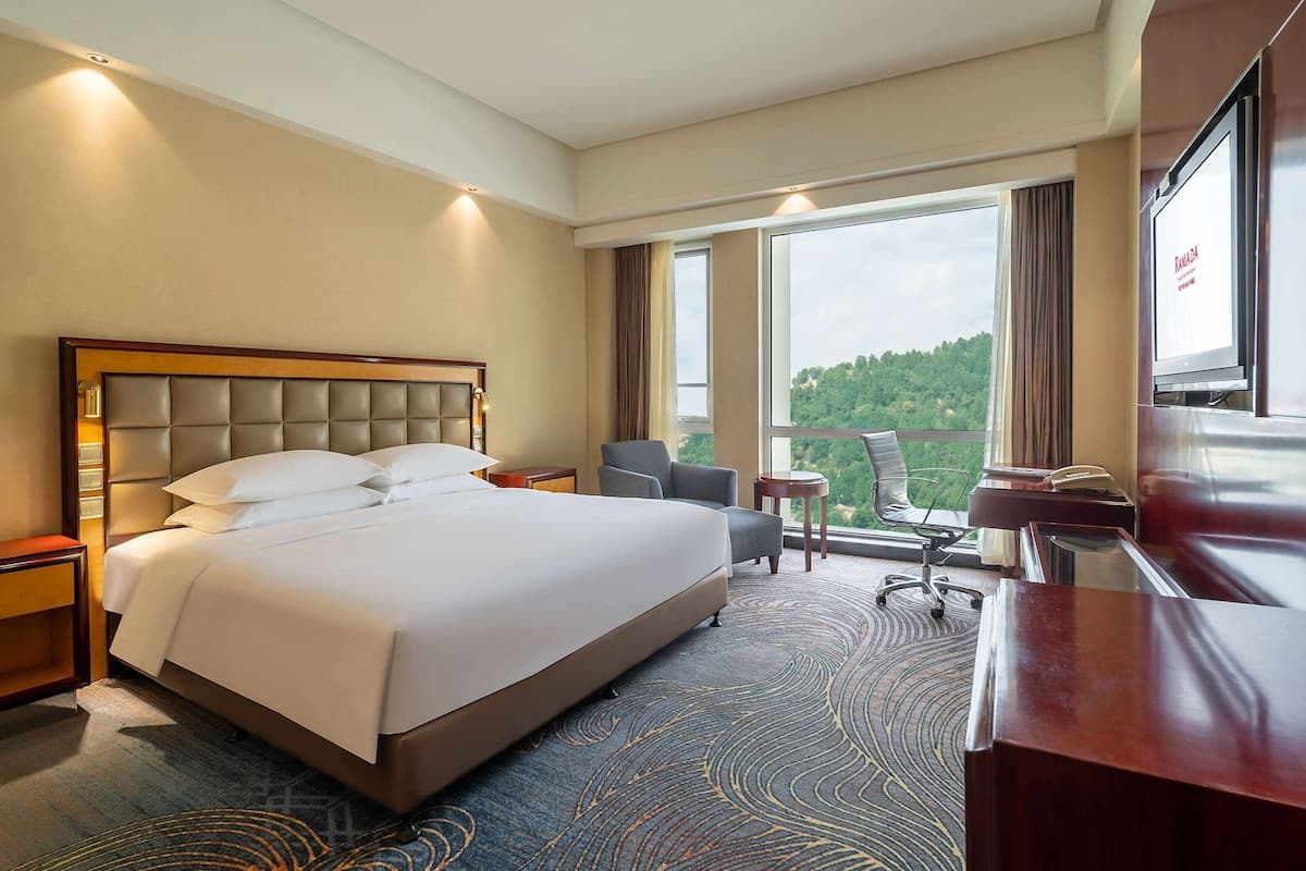 A hotel room with a large bed, a desk, a chair, and a TV.