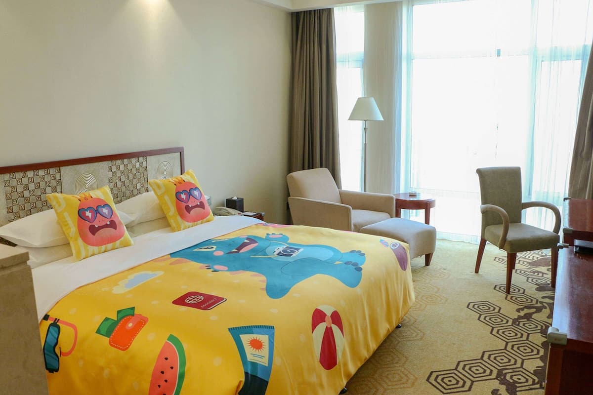A hotel room with a large bed, a chair, a desk, and a window with curtains.