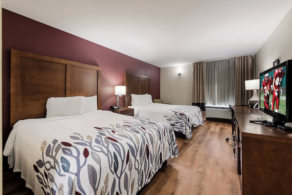 A hotel room with two beds, a television, and a desk with a lamp.
