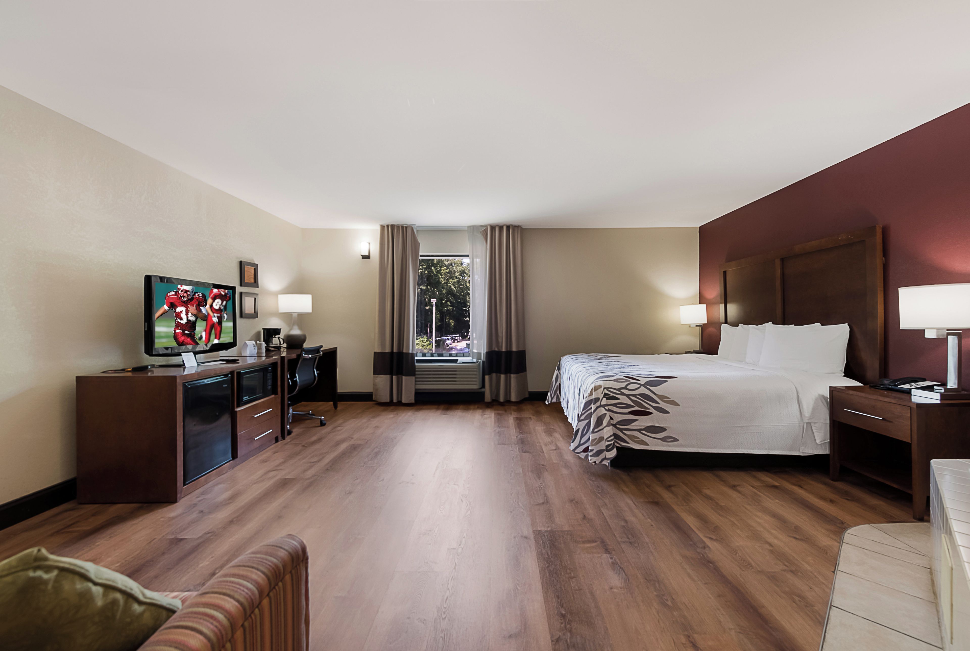 Une chambre d’hôtel comprenant un lit, un bureau avec une télévision, une chaise, une table de chevet et une fenêtre avec des rideaux.