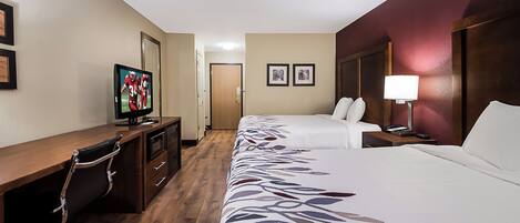 A hotel room with a desk, two beds, a TV, and a bedside lamp.