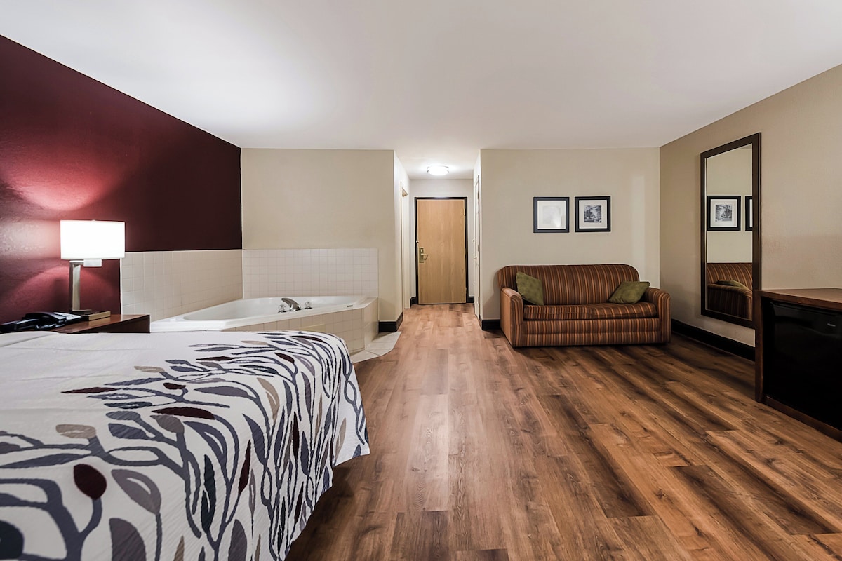 Ett hotellrum med en stor säng, en sittgrupp med soffa, badkar och trägolv.