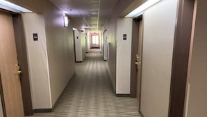 A hotel hallway with carpeted floors, doors on both sides, and overhead lighting.