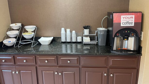 Una estación de café con una máquina de café, dispensadores de condimentos y un soporte para tazones.