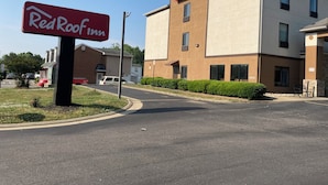 Un hotel Red Roof Inn con fachada moderna, un estacionamiento y cielo despejado.