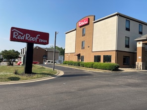 Un hotel Red Roof Inn con fachada moderna, un estacionamiento y cielo despejado.