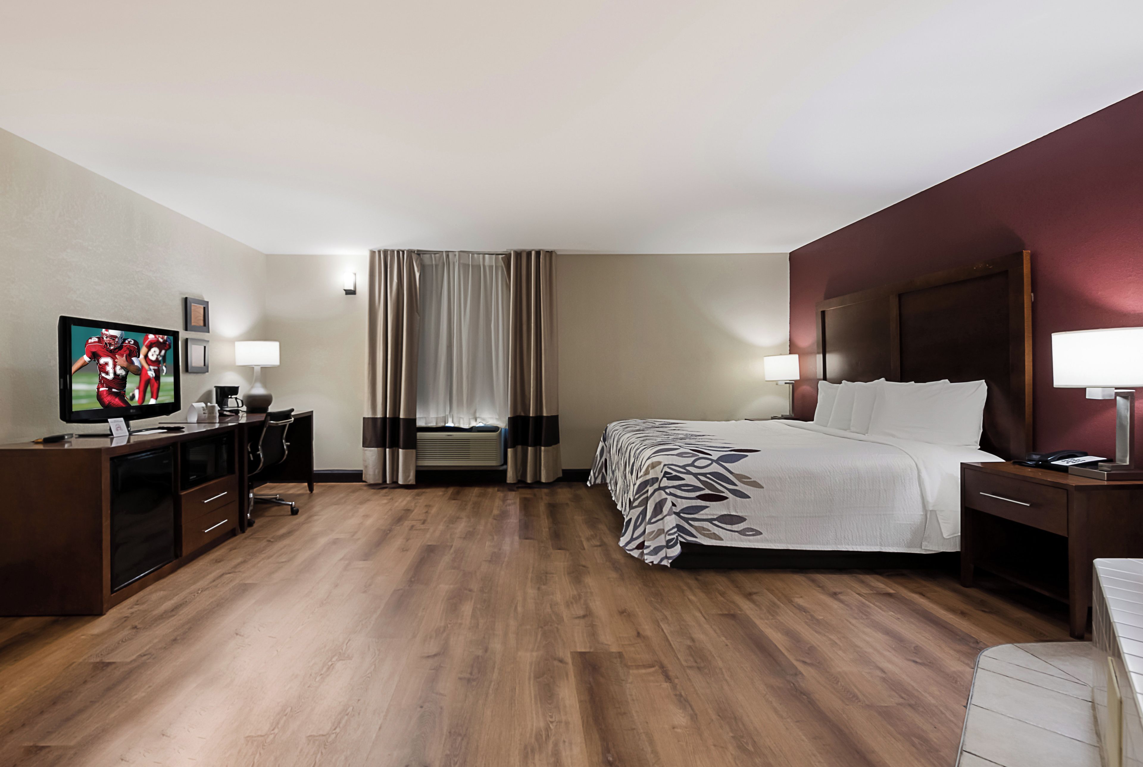 A hotel room with a bed, bedside tables, a desk with a television, and a window with curtains.
