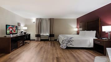 A hotel room with a bed, bedside tables, a desk with a television, and a window with curtains.