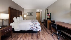 Habitación de hotel con cama, lámparas de noche, un escritorio con silla, televisor y cuadros en la pared.