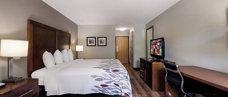 Une chambre d’hôtel avec un lit, des lampes de chevet, un bureau avec une chaise, une télévision et des tableaux encadrés au mur.