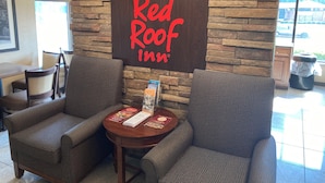 A Red Roof Inn reception area with a stone wall backdrop, two armchairs, a small table with brochures, and a trash can.