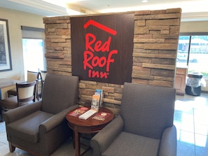 A Red Roof Inn reception area with a stone wall backdrop, two armchairs, a small table with a menu, and a trash can.