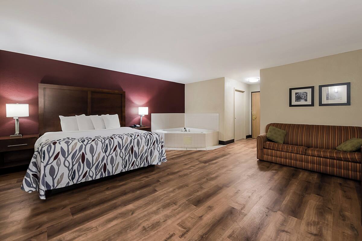 A hotel room with a bed, a sofa, a bathtub, and a wall with framed pictures.