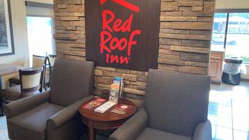 A Red Roof Inn reception area with a stone wall backdrop, two armchairs, a small table with brochures, and a trash can.