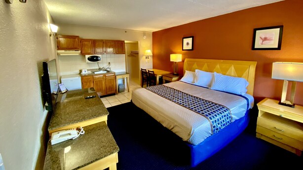 Habitación de hotel con cama, escritorio, silla, microondas, lavamanos y un pequeño cubo de basura.