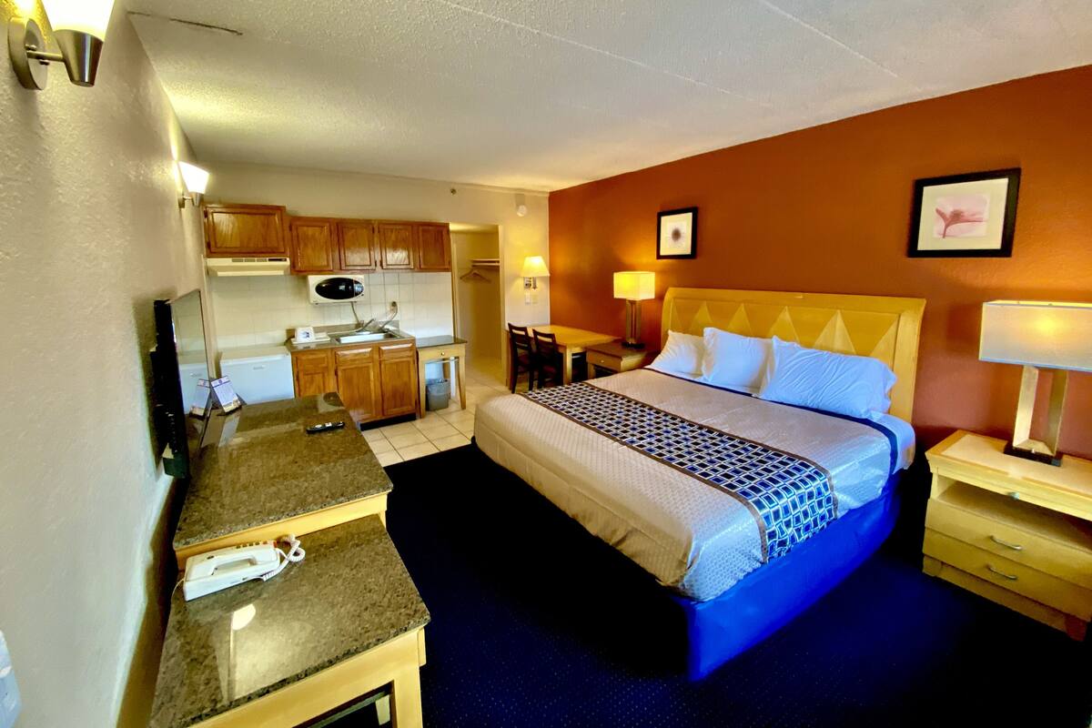 A hotel room with a bed, a desk, a chair, a microwave, a sink, and a small trash bin.