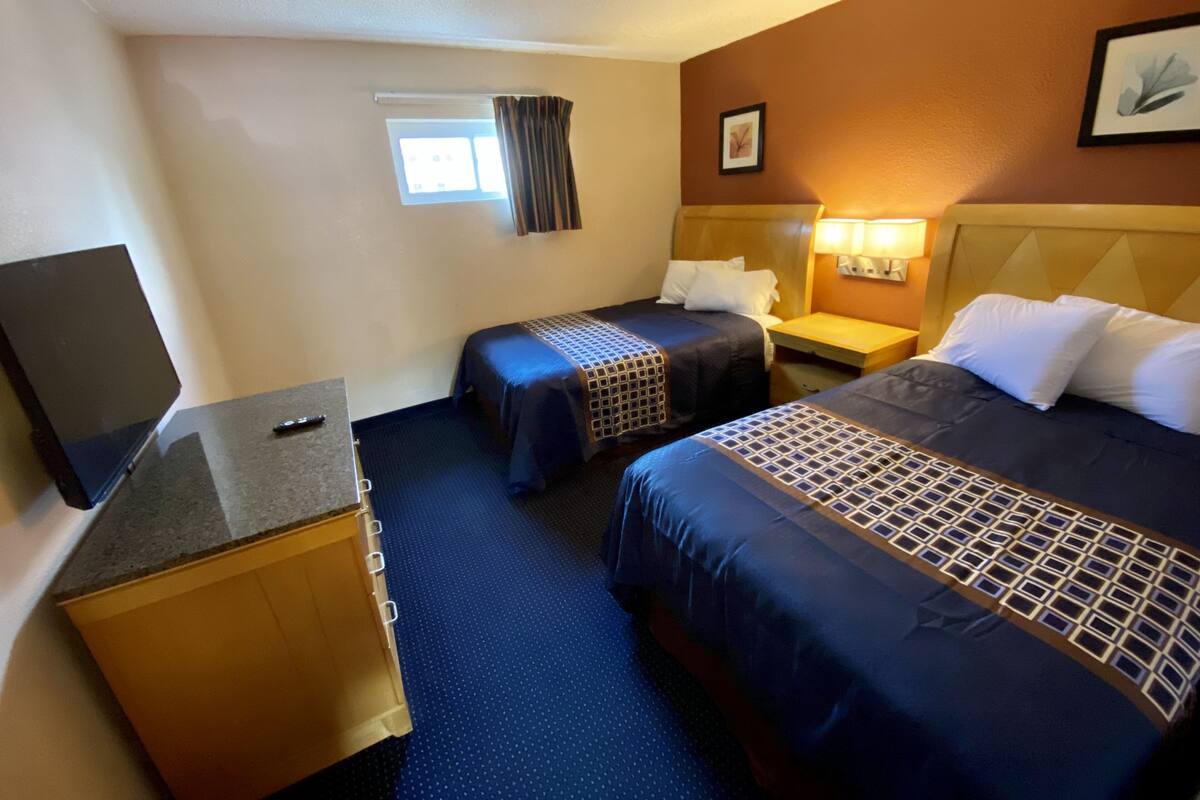 A hotel room with two beds, a desk, a television, and a window with curtains.