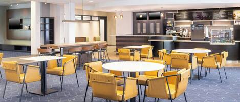 A modern restaurant with round tables and yellow chairs, a bar area, and a menu board.