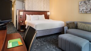 A hotel room with a bed, a TV, a desk with a chair, a sofa, and a wall with a painting. - Courtyard by Marriott Hanover Lebanon (Lebanon)