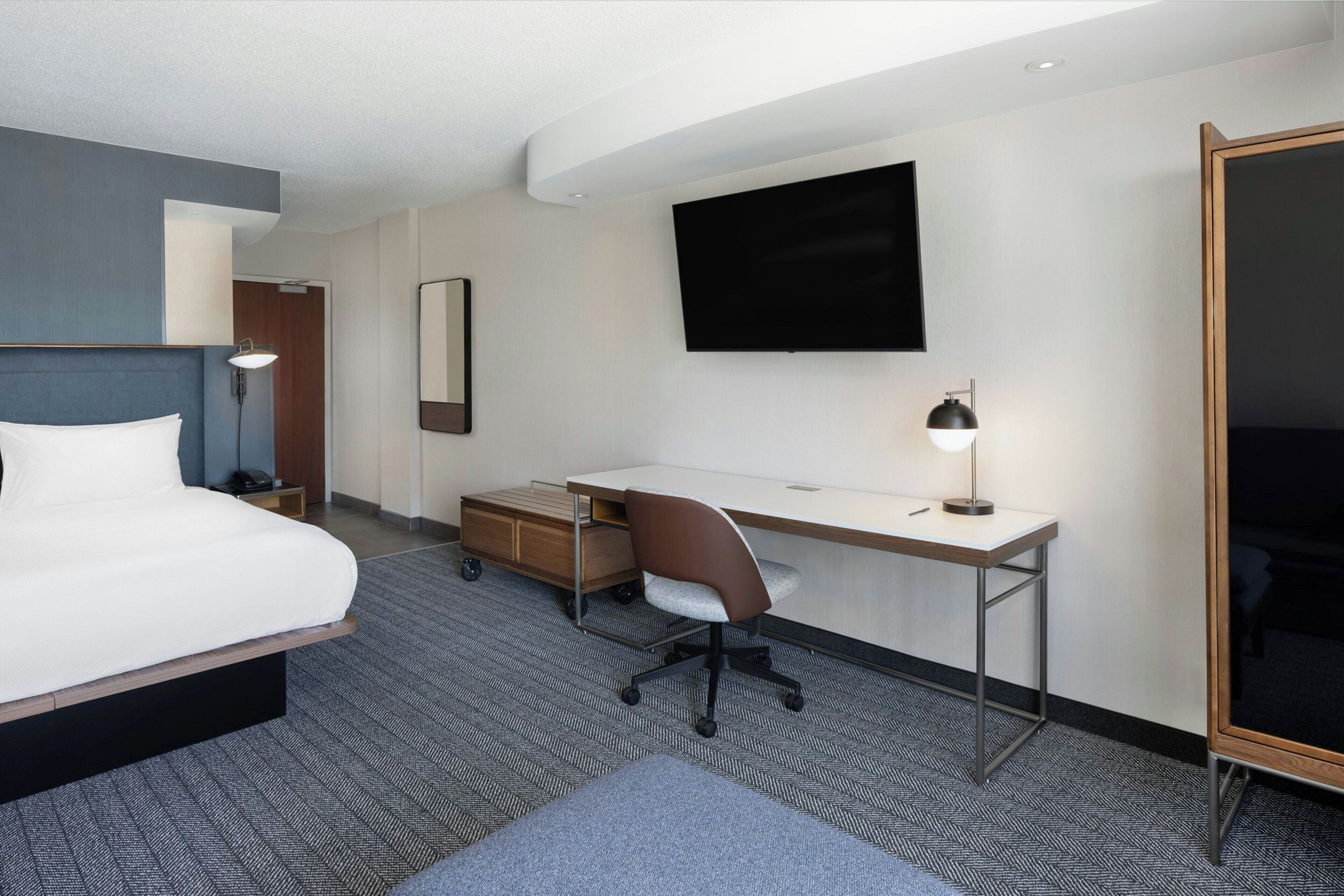 A hotel room with a bed, desk, chair, and a TV mounted on the wall.