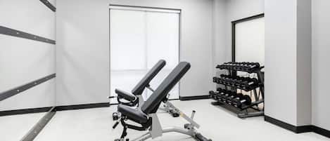 A gym with a bench press, dumbbells, and a door.