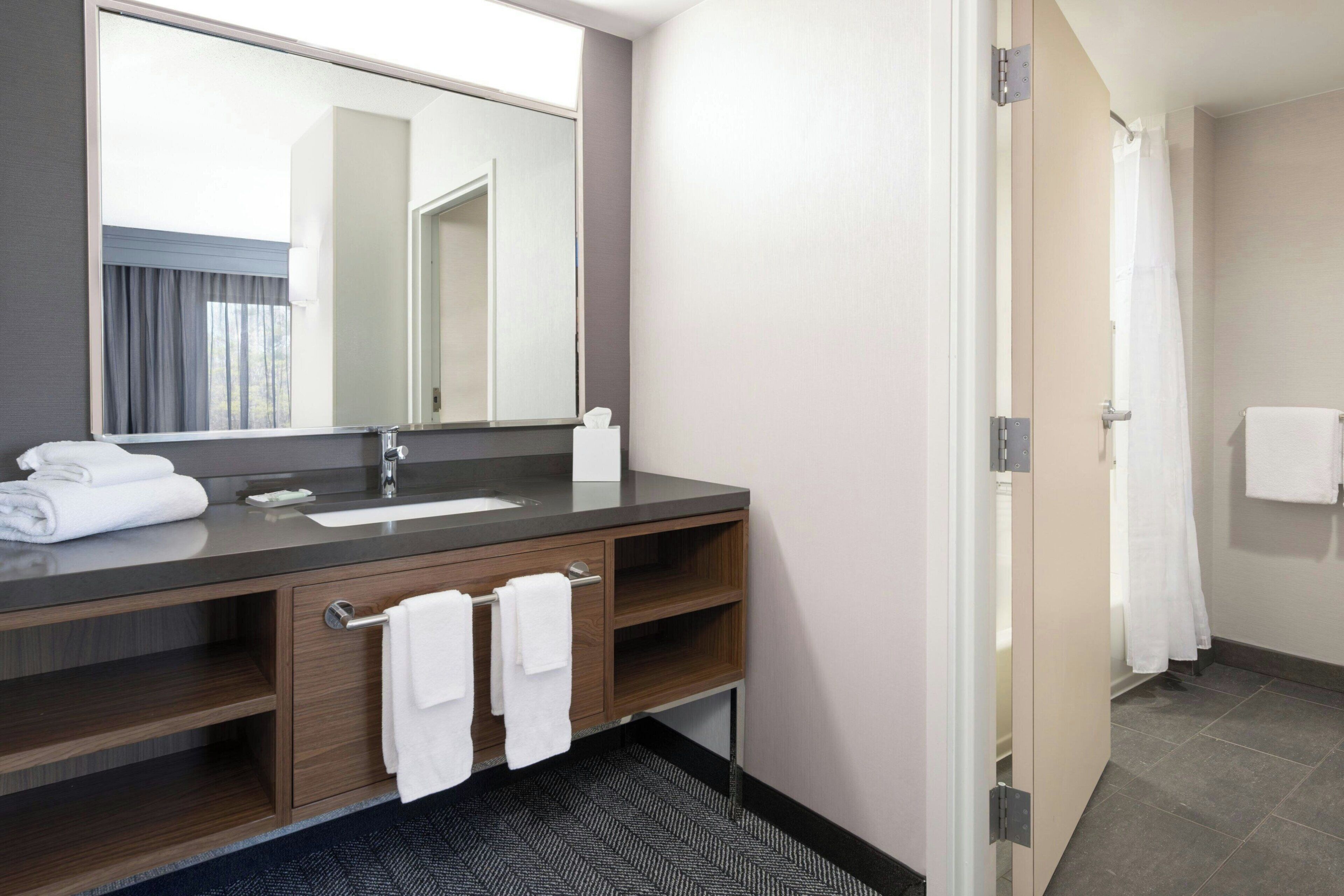 A modern bathroom with a dark wood vanity, a large mirror, a white sink, and a shower area.