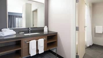A modern bathroom with a dark wood vanity, a large mirror, a white sink, and a shower area.