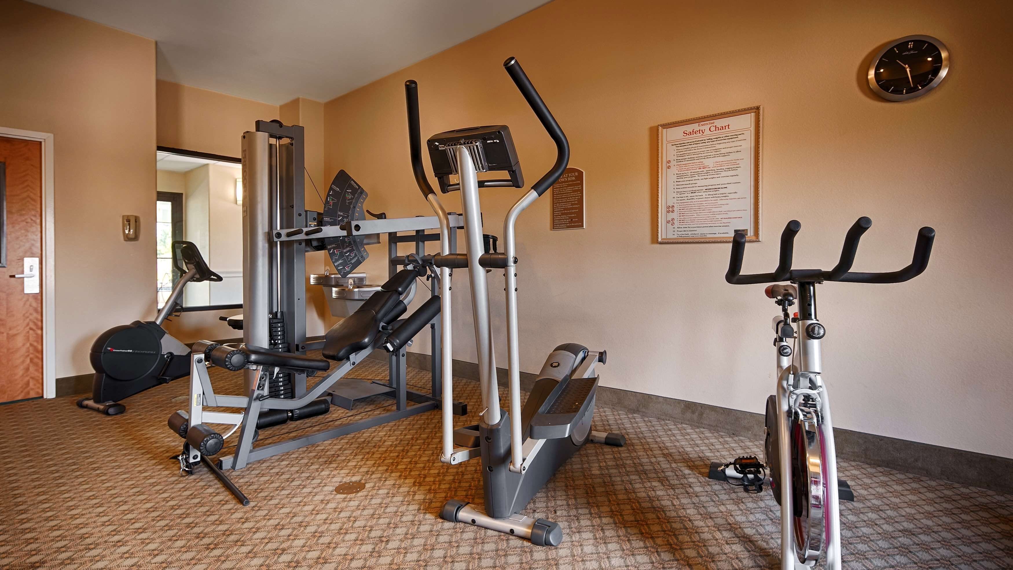 Une salle de sport équipée de divers appareils d’exercice, notamment un tapis de course, un vélo elliptique et des appareils de musculation.