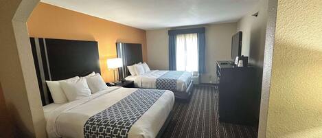A hotel room with two beds, a desk, a television, and a window with curtains.