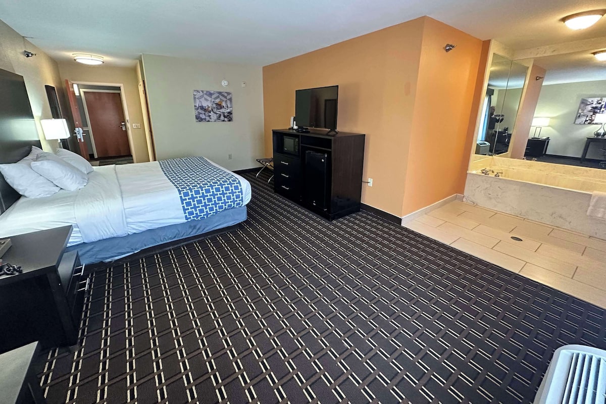 Ein Hotelzimmer mit einem Bett, einem Schreibtisch, einer Kommode, einem Fernseher und einem Badezimmer mit Waschbecken und Spiegel.