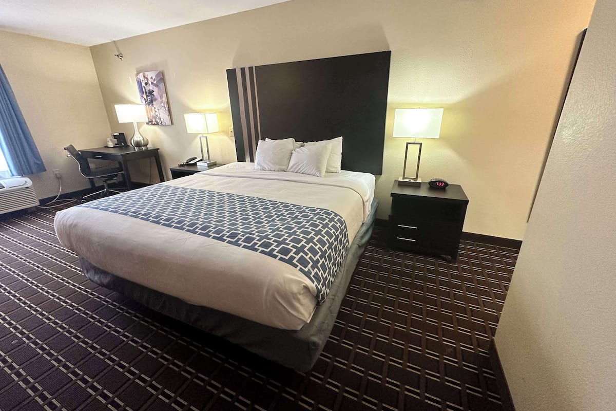 Ein Hotelzimmer mit einem großen Bett, einem Schreibtisch, zwei Nachttischen und einem an der Wand befestigten Fernseher.