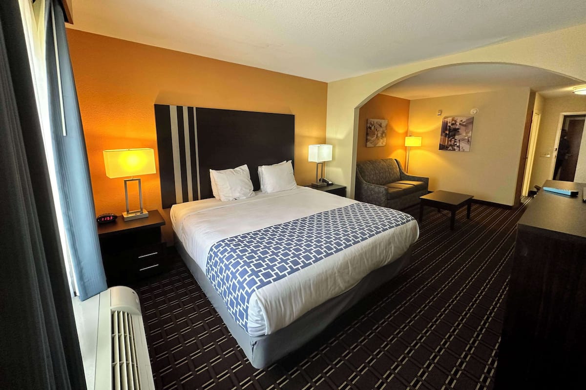 Ein Hotelzimmer mit einem großen Bett, zwei Nachttischen, einem Sessel, einem Schreibtisch und einem an der Wand befestigten Fernseher.