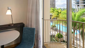 A balcony with a view of a swimming pool, palm trees, and a high-rise building.
