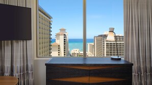 A hotel room with a large window offering a view of the ocean and high-rise buildings.