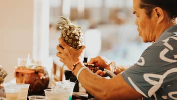 Une personne tenant un ananas dans un bar, avec des boissons et une noix de coco posée sur le comptoir.