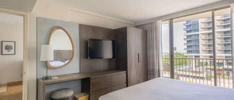 A modern hotel room with a large bed, a flat-screen TV, a desk with a lamp, and a view of a high-rise building.