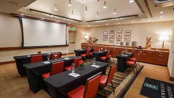 A conference room with tables, chairs, a projector screen, and a buffet area.