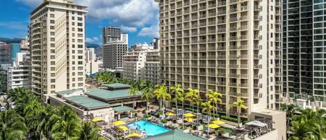 A high-rise hotel with a rooftop pool, palm trees, and modern architecture.